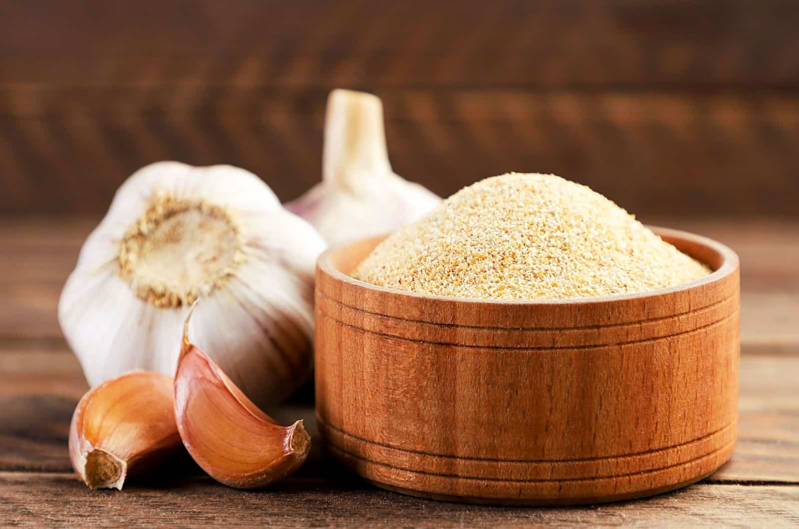 Ground garlic in a plate and cloves on a wooden