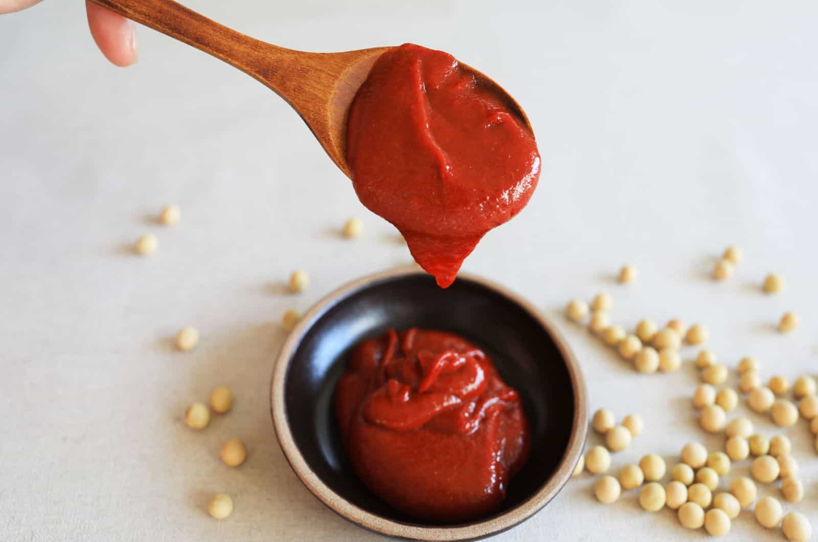 La comida coreana Gochujang(pasta de pimiento rojo) se vierte de una cuchara de madera en un tarro