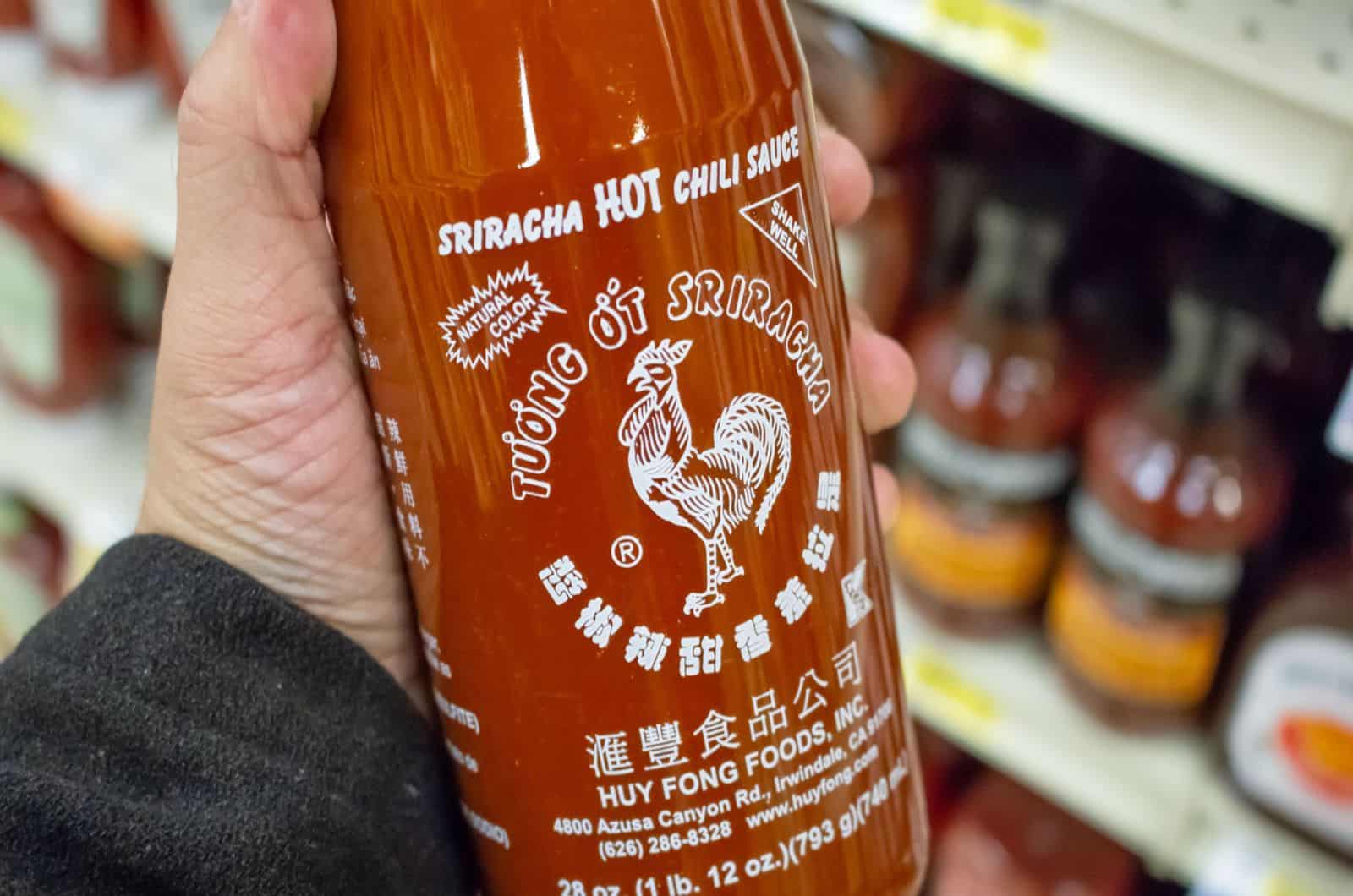 in der Hand eine Flasche Sriracha-Chili-Sauce