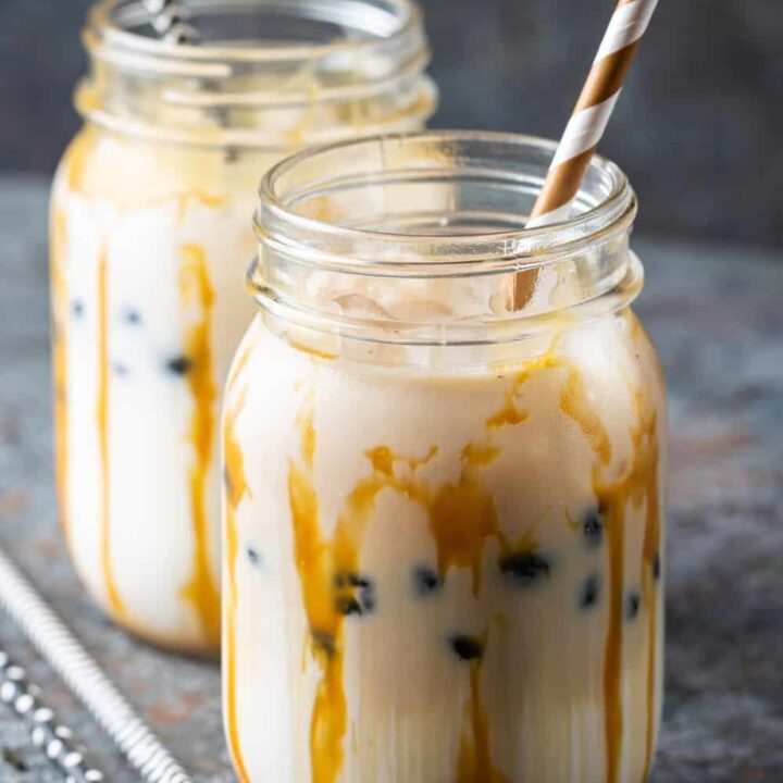 Té de burbujas cremoso marrón claro con leche y tapioca negra en un tarro de cristal sobre fondo gris