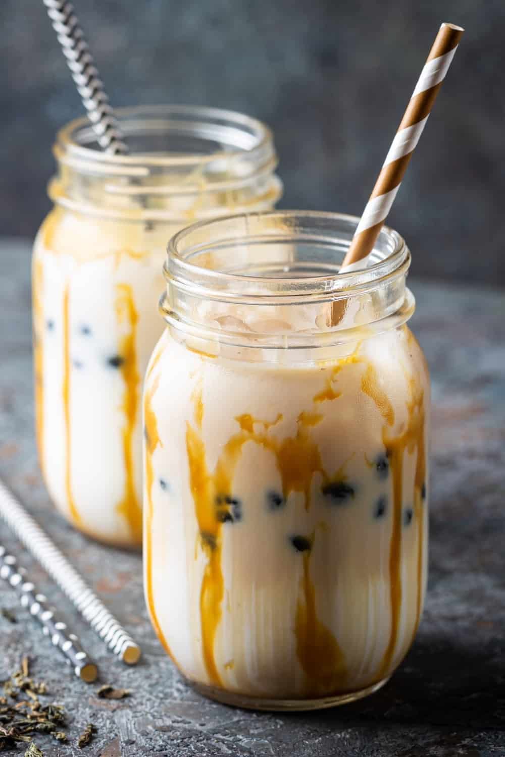 Té de burbujas cremoso marrón claro con leche y tapioca negra en un tarro de cristal sobre fondo gris