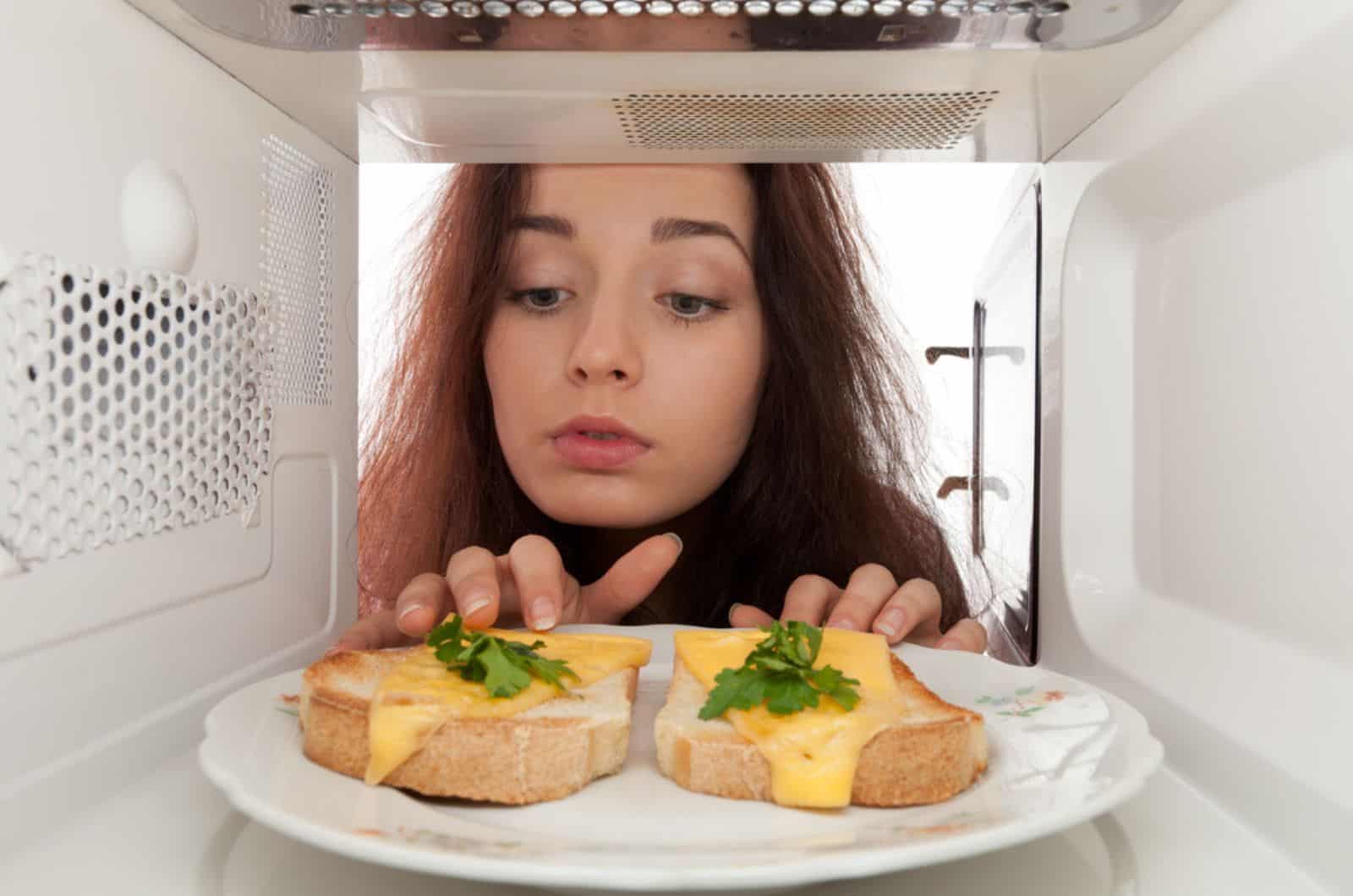 woman checking bread with cheese in a microwave