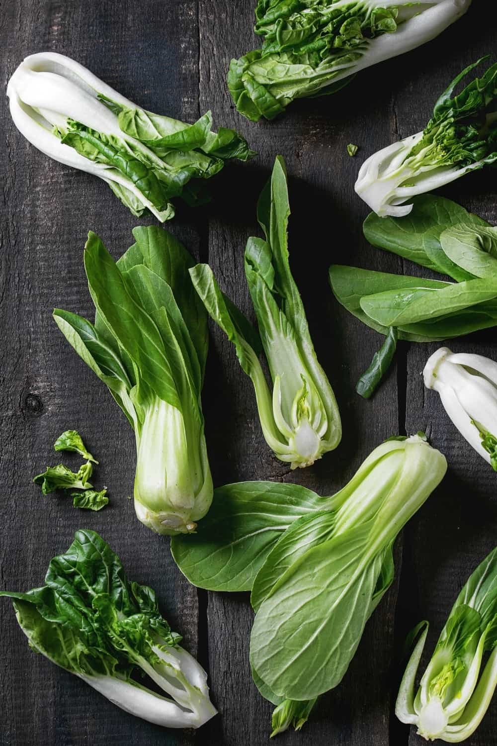 Assortment of whole and sliced raw baby bok choy (Chinese cabbage) over old wooden background.