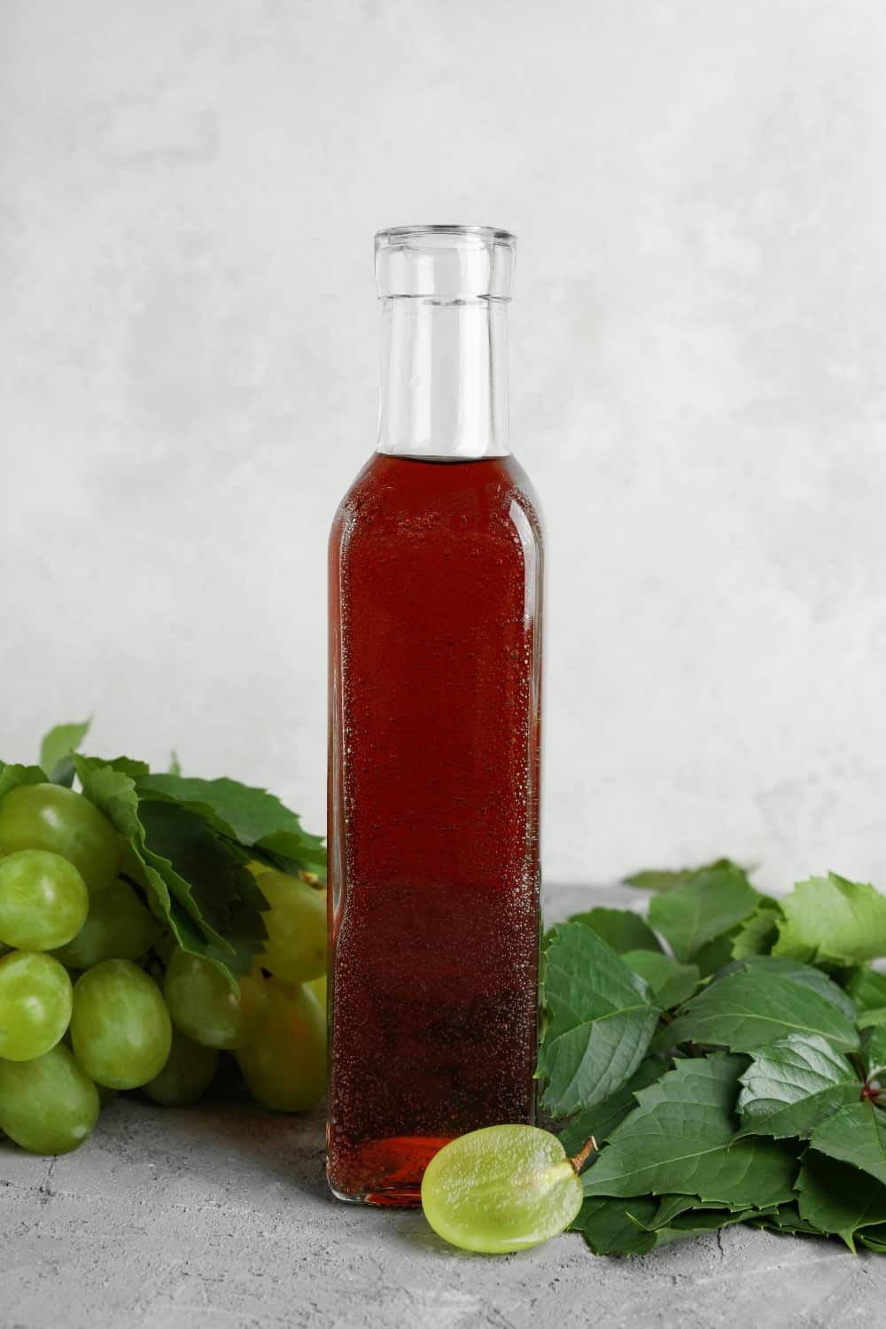 Botella de vinagre, uva y hojas sobre mesa de textura gris