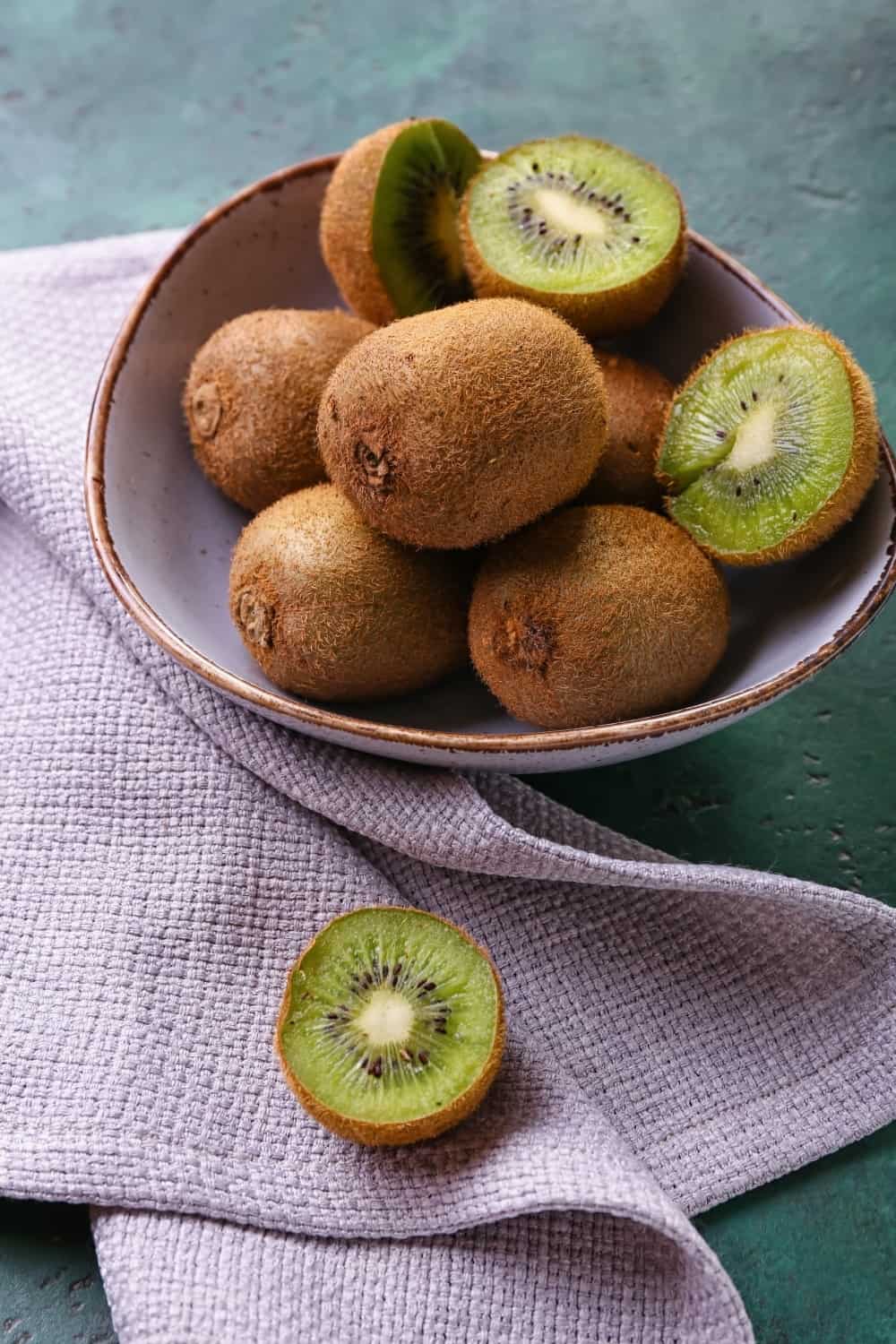 Bowl with fresh kiwi on green background