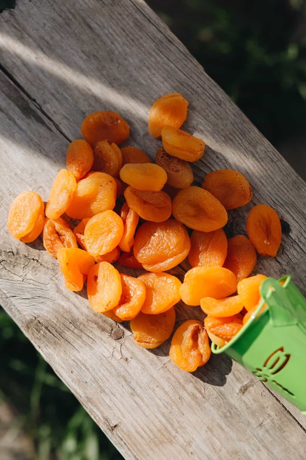 Dried apricots spilled out of a green bucket on a wooden background