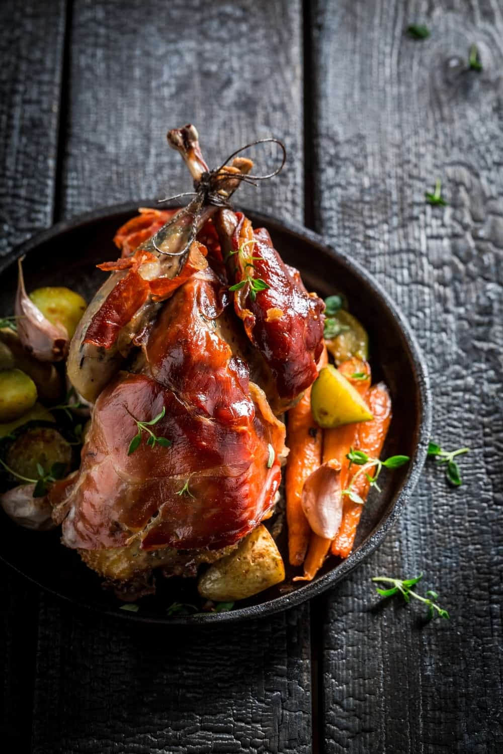 Faisán a la parrilla con bacon y verduras sobre fondo oscuro