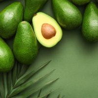 Fresh avocados and palm leaves on color background