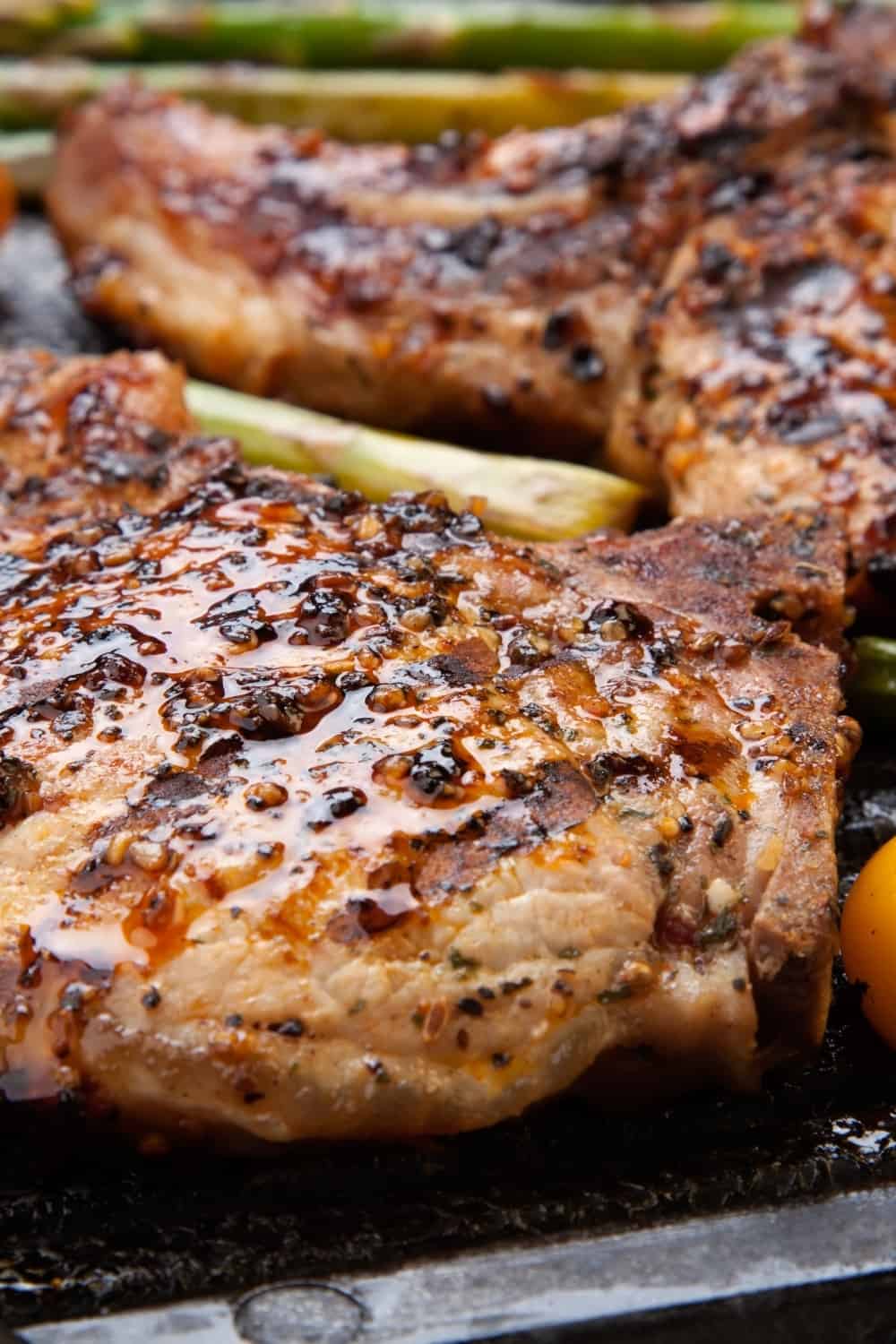 Juicy pork chops are grilled on griddle with asparagus and bell pepper.