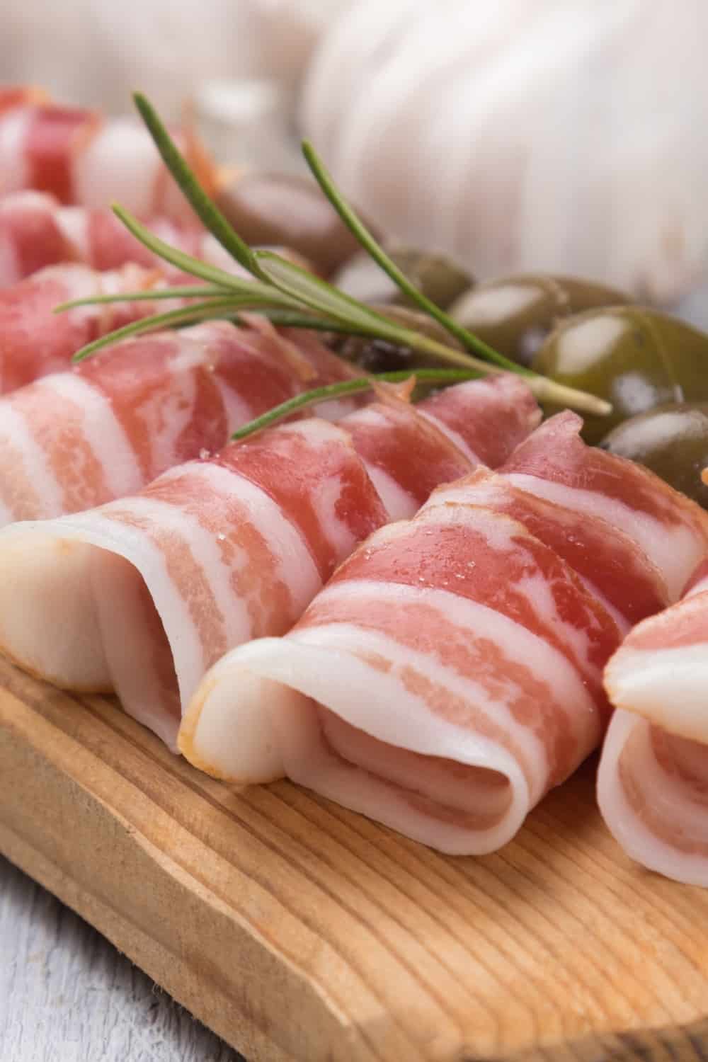 Involtini di pancetta serviti con olive in salamoia,