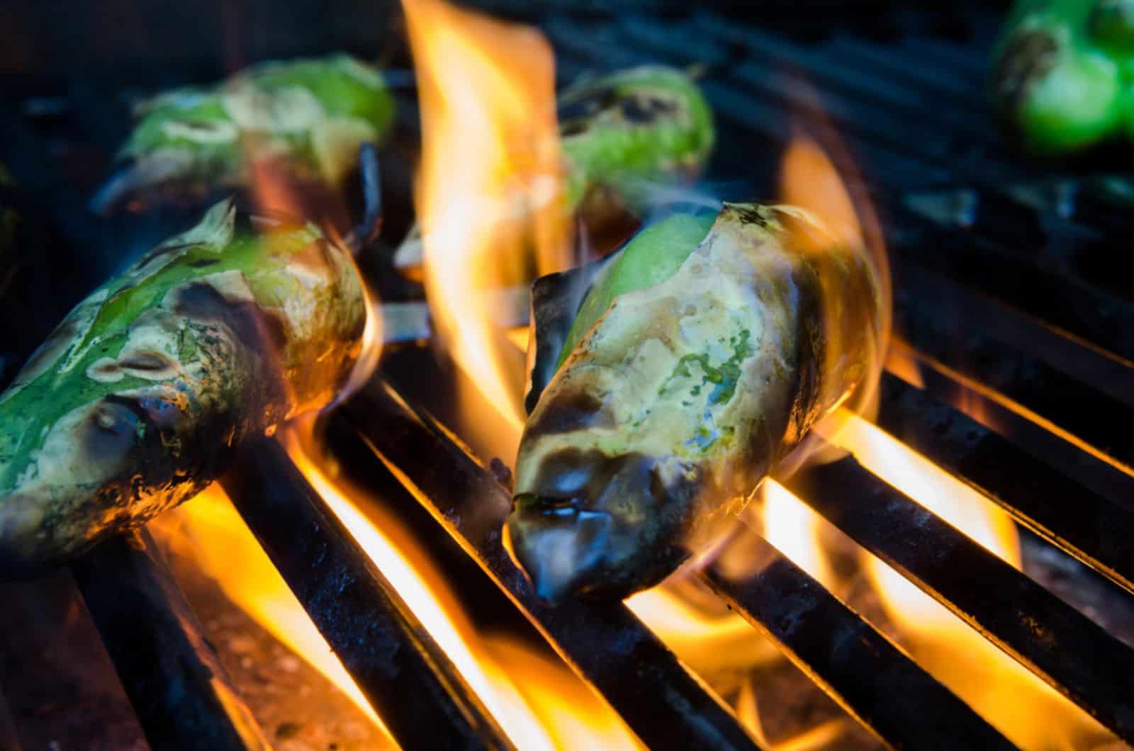 Small green peppers roast on flames on a grill