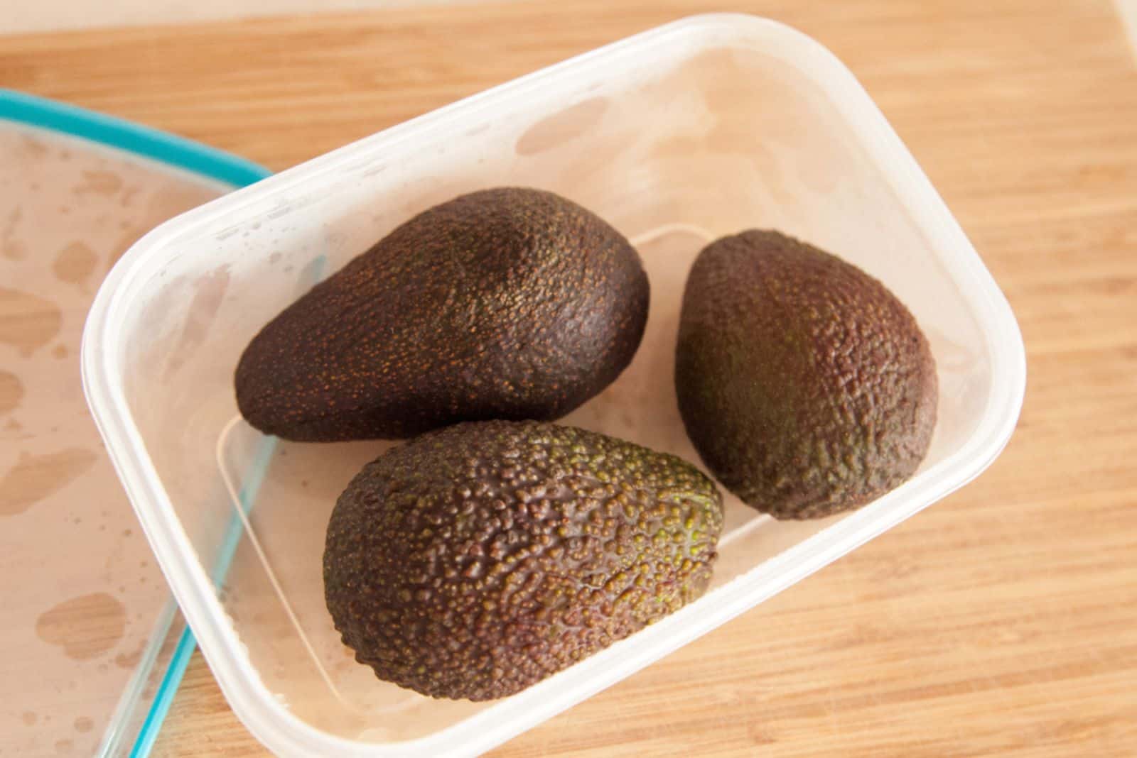 Tres aguacates enteros en un recipiente de plástico sobre la encimera - para guardar en el frigorífico