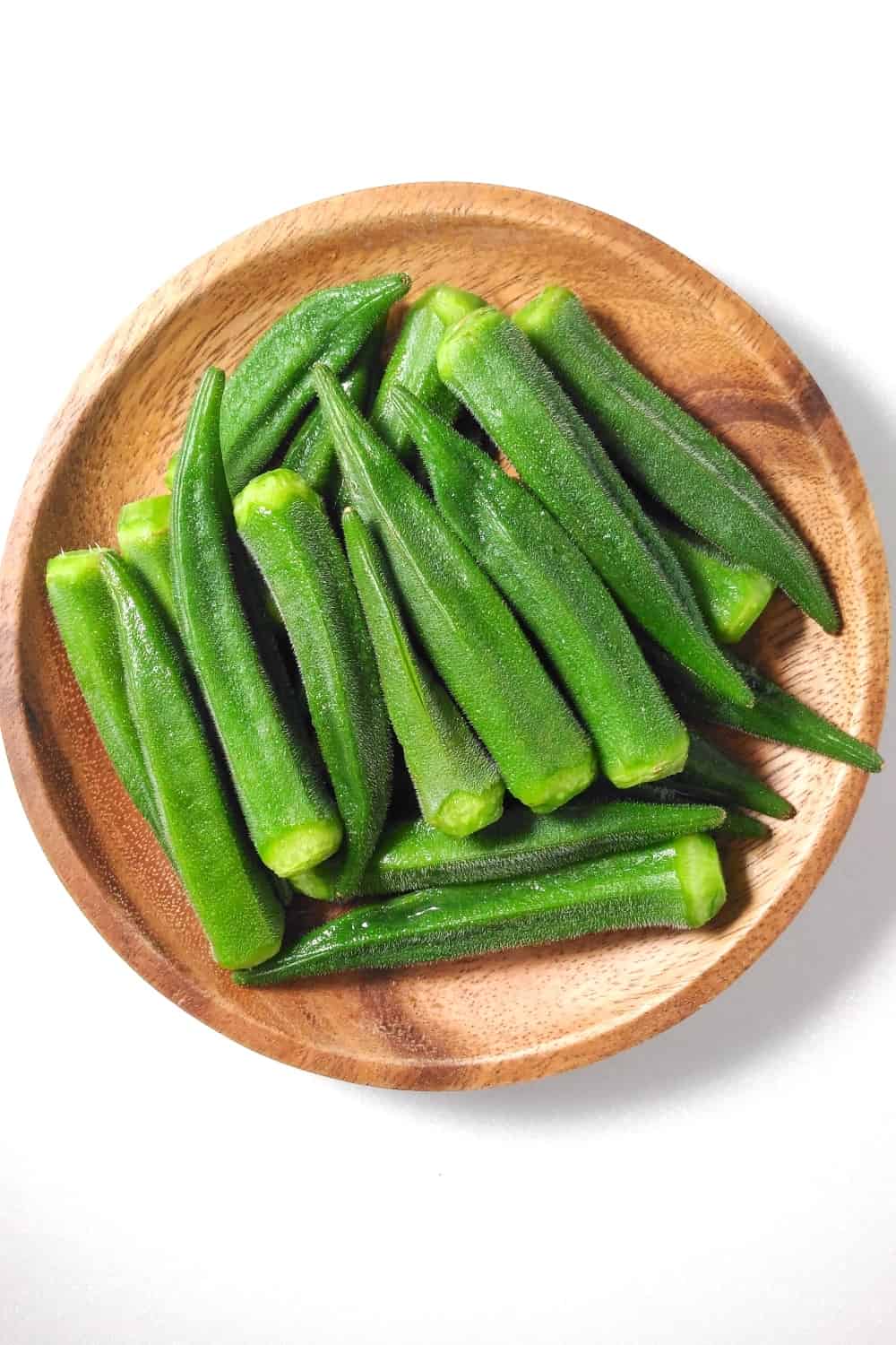 Top view of pile of fresh green okra on wooden plate