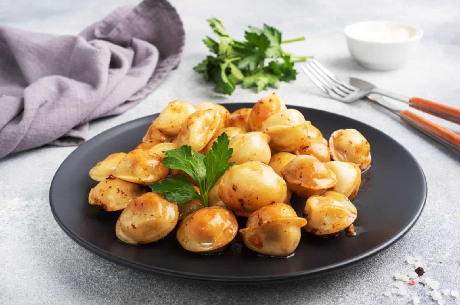 Traditionelle gebratene Pelmeni, Ravioli, mit Fleisch gefüllte Knödel auf schwarzem Teller