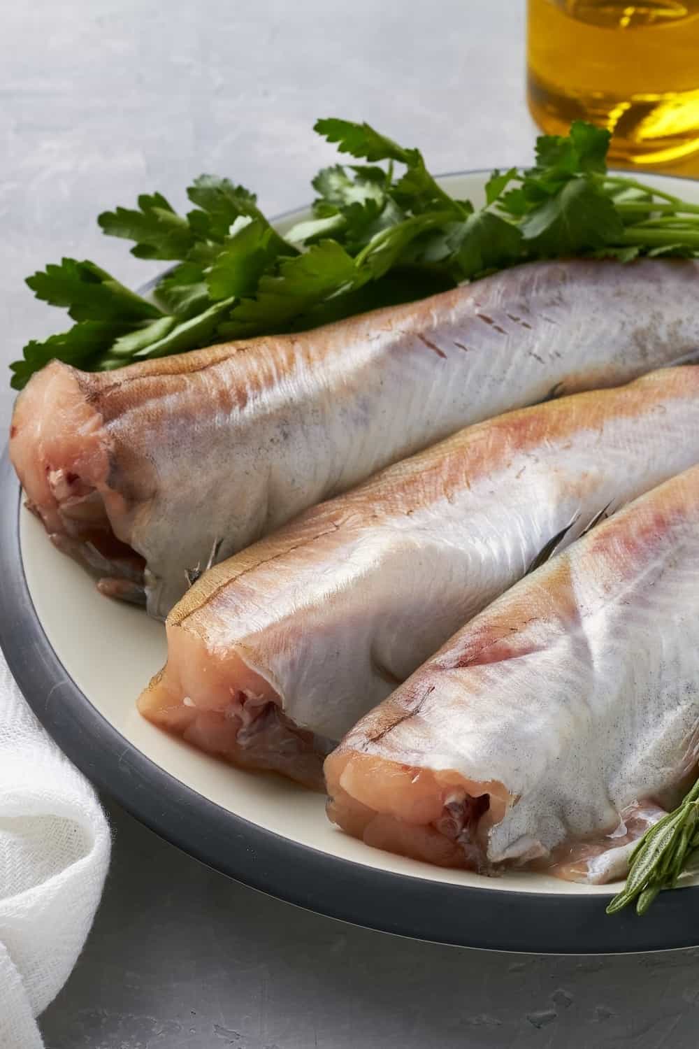 raw pollock fish on plate lemon parsley rosemary grey background