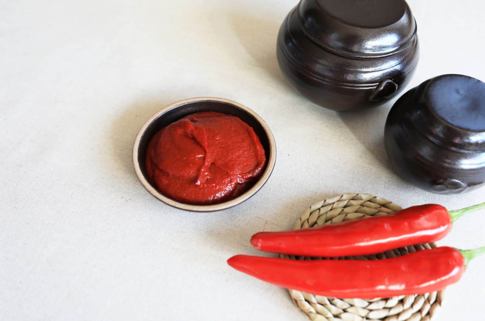 red pepper paste in a jar with raw red pepper and soybeans on white floor