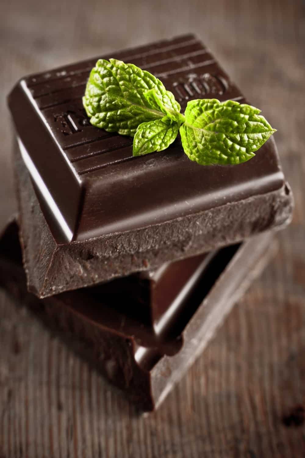 stack of chocolate pieces with a leaf of mint on wooden background
