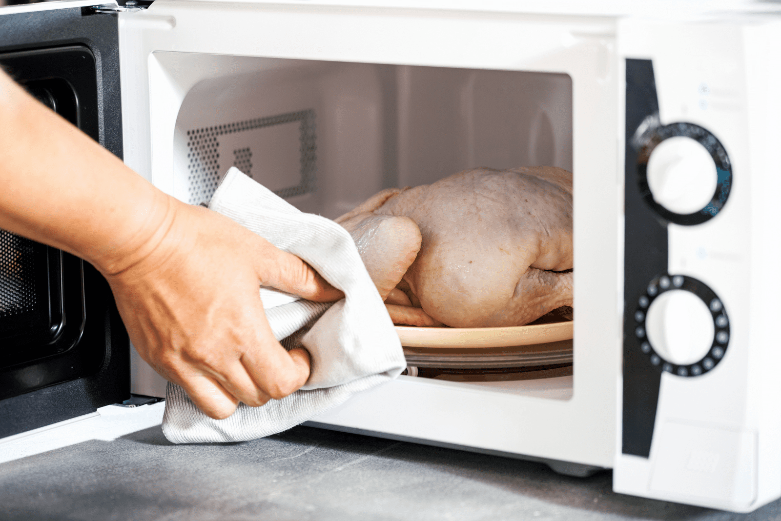 the woman takes the defrosted chicken out of the microwave
