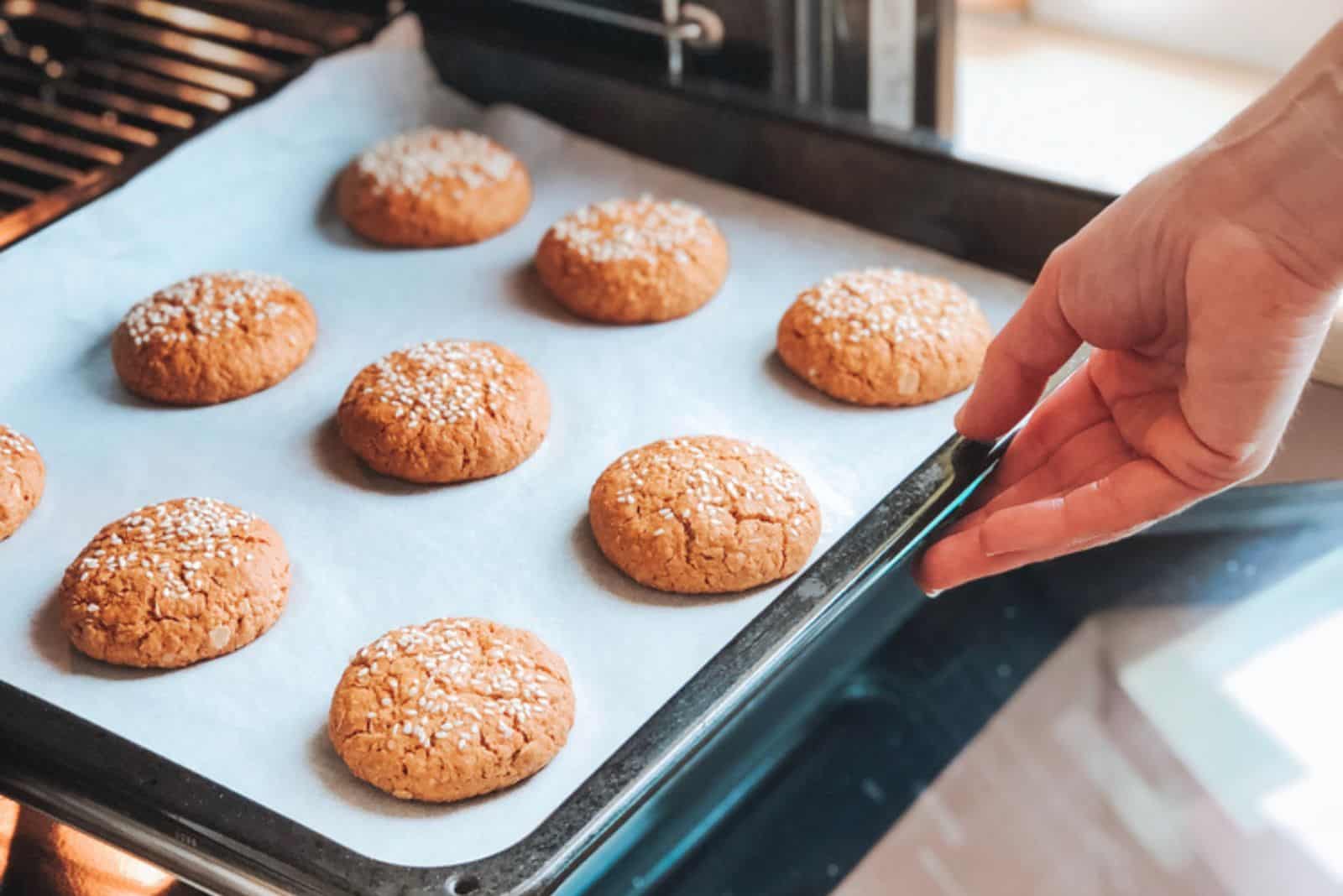 A woman puts in the oven a baking tray with oatmeal cookies