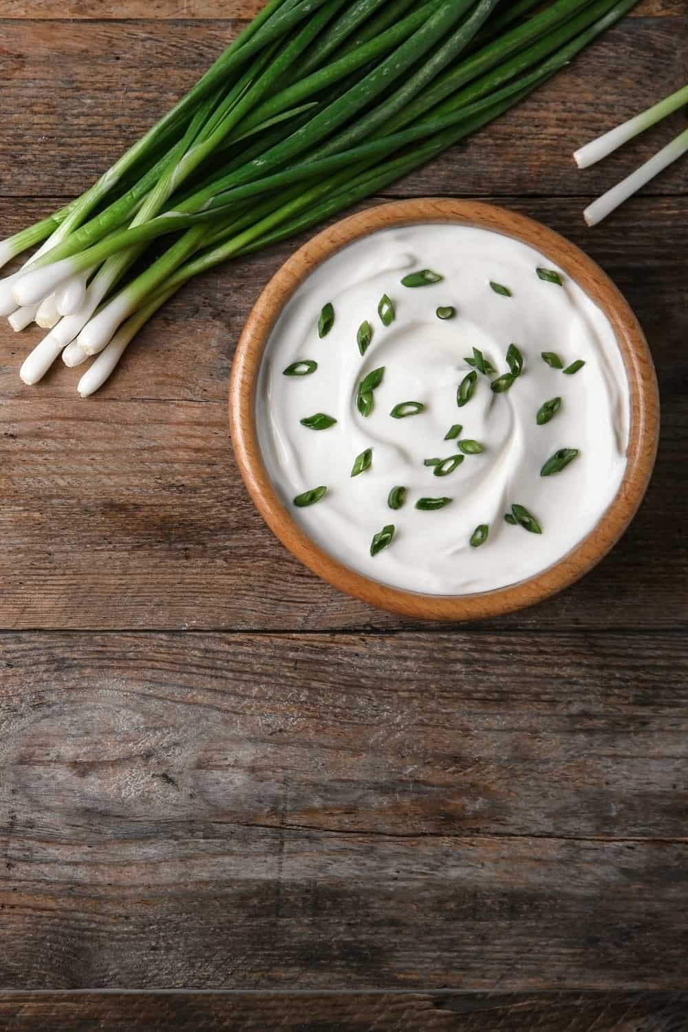 Schüssel mit saurer Sahne mit grünen Zwiebeln und Löffel auf dem Holztisch