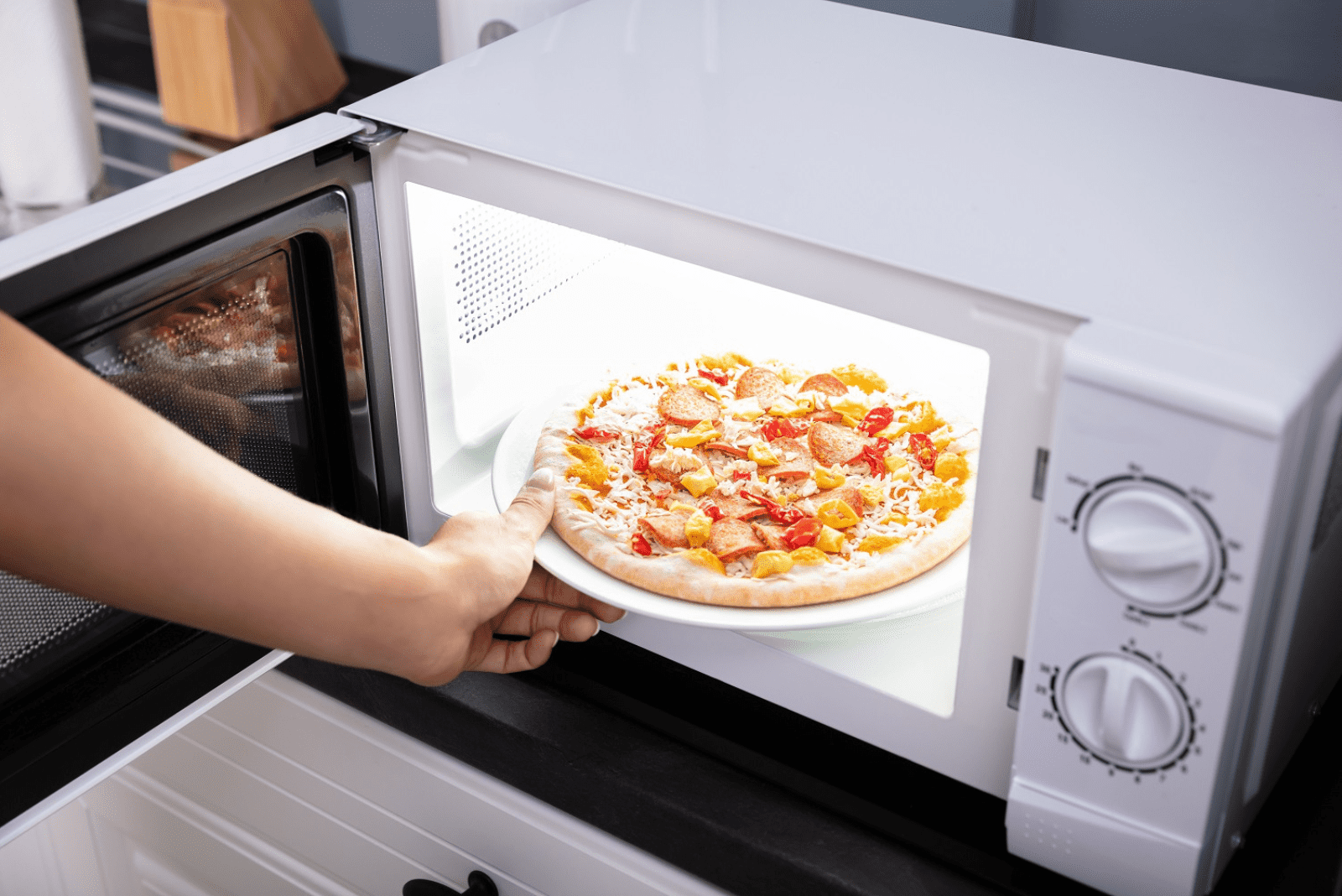 the woman puts the pizza in the microwave