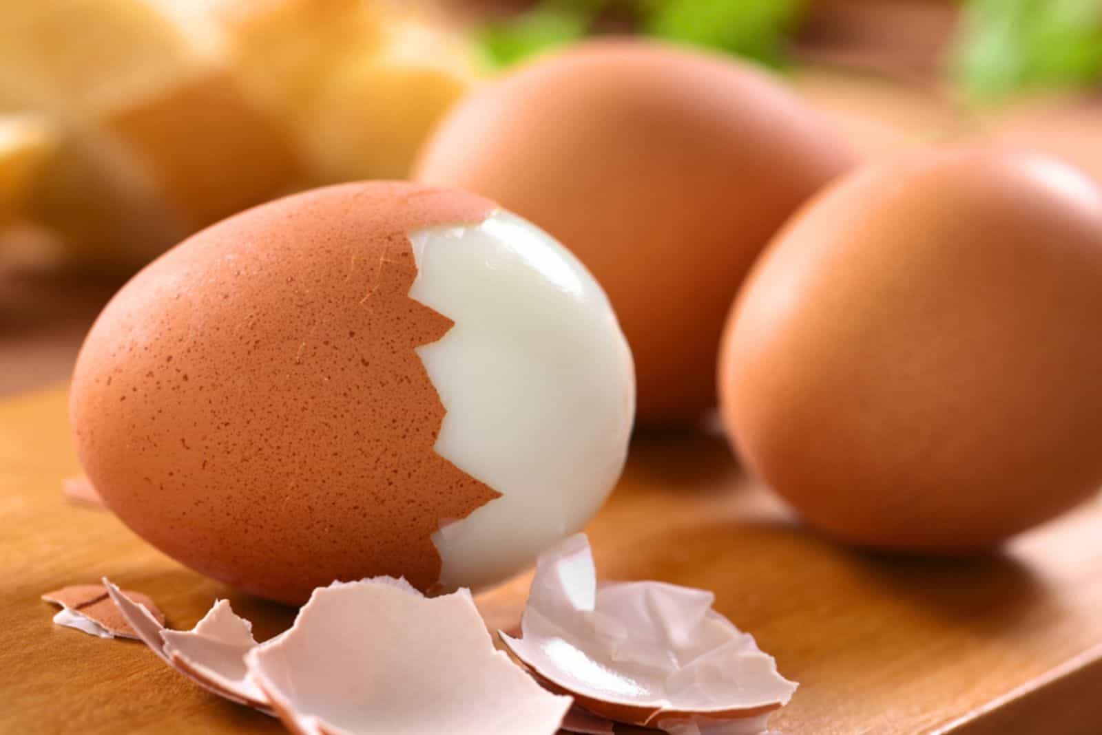 Fresh hard boiled eggs with shell beside on wooden board