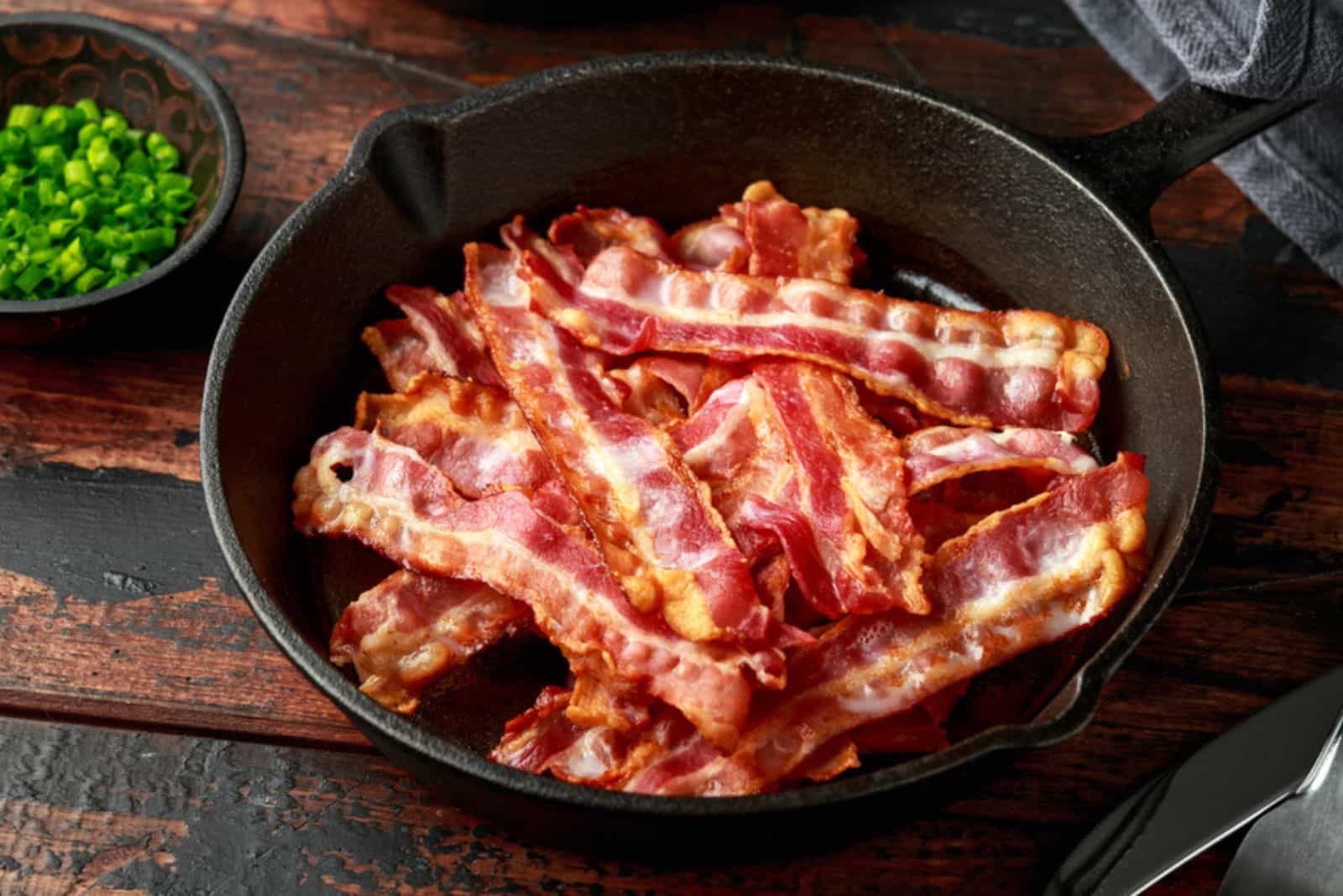 Pezzi croccanti di pancetta streaky fritti in una padella di ghisa