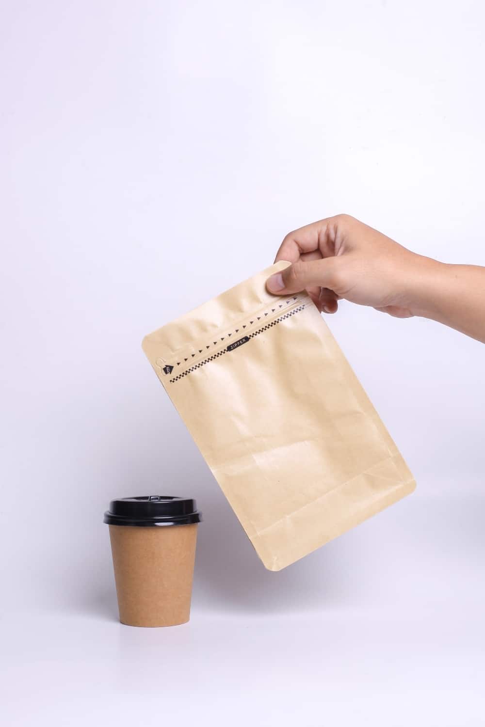 Hände halten Kaffeebeutel Tasche mit Reißverschluss und stehend Pappbecher isoliert auf weißem Hintergrund
