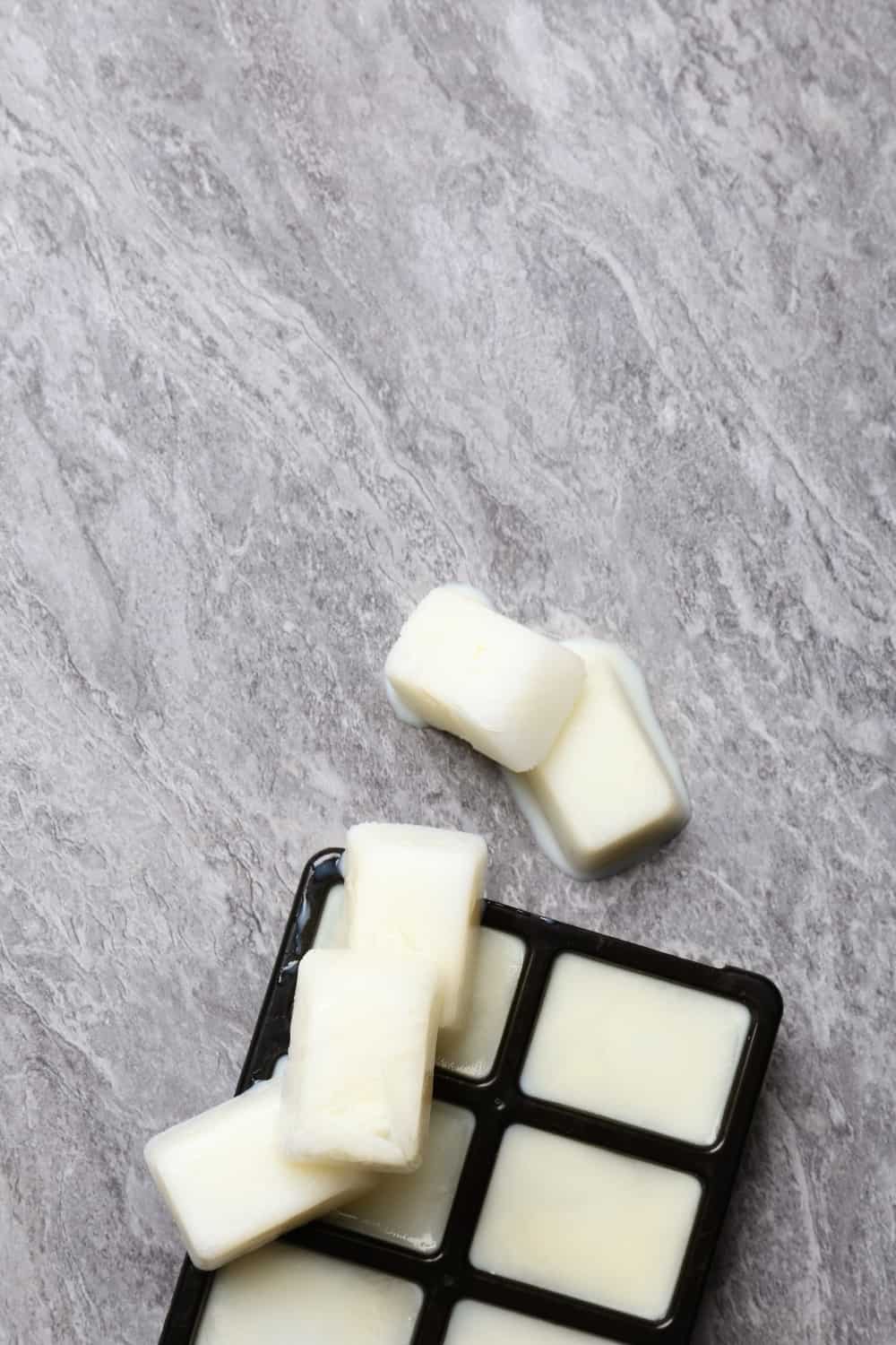 Ice cubes made with milk and tray on grey background
