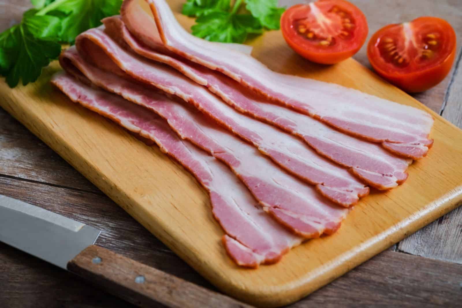 Raw sliced bacon on wooden board
