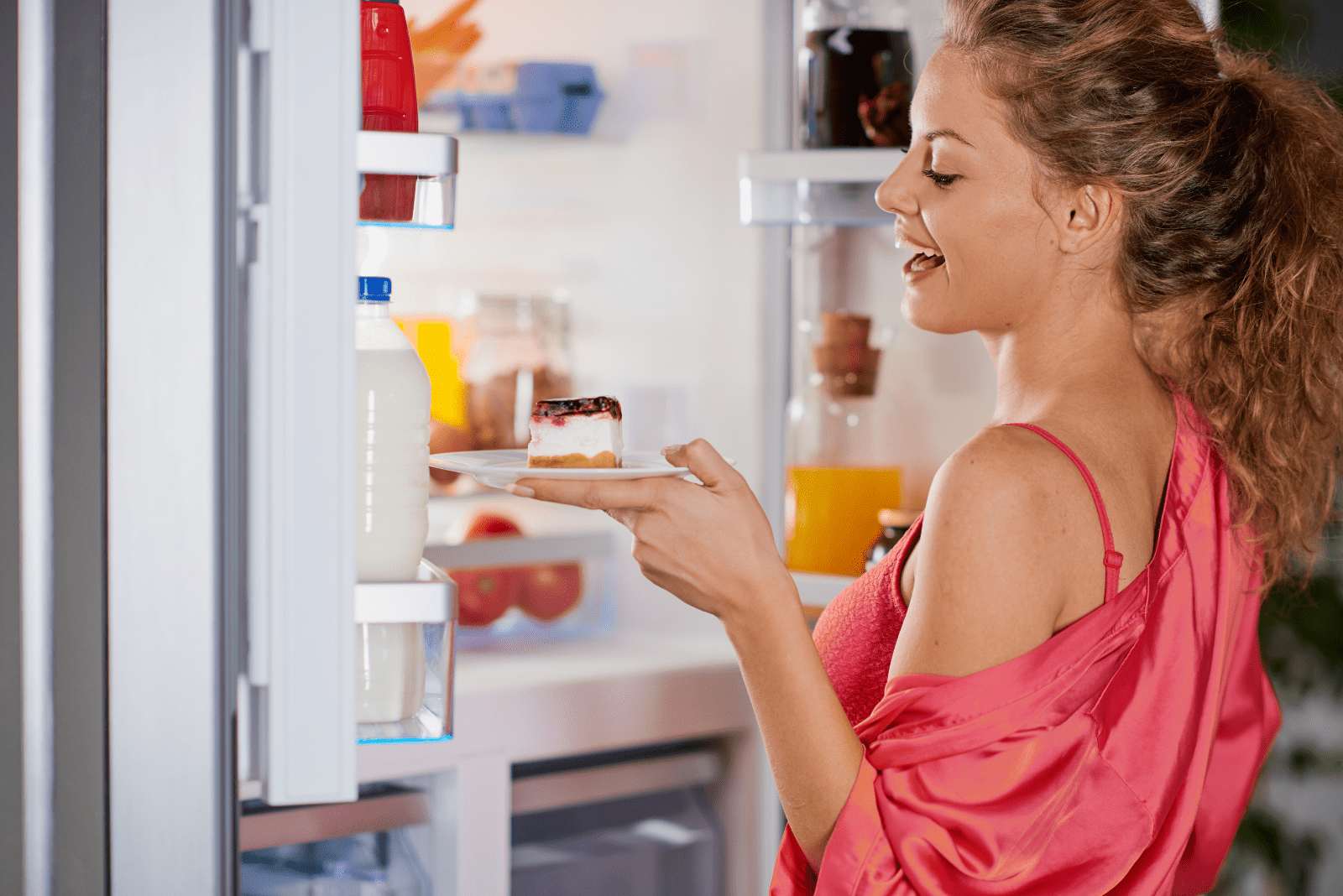a smiling woman takes a cake from the fridge