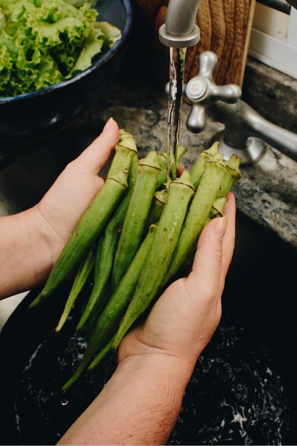 una mujer lava okra fresca bajo el grifo