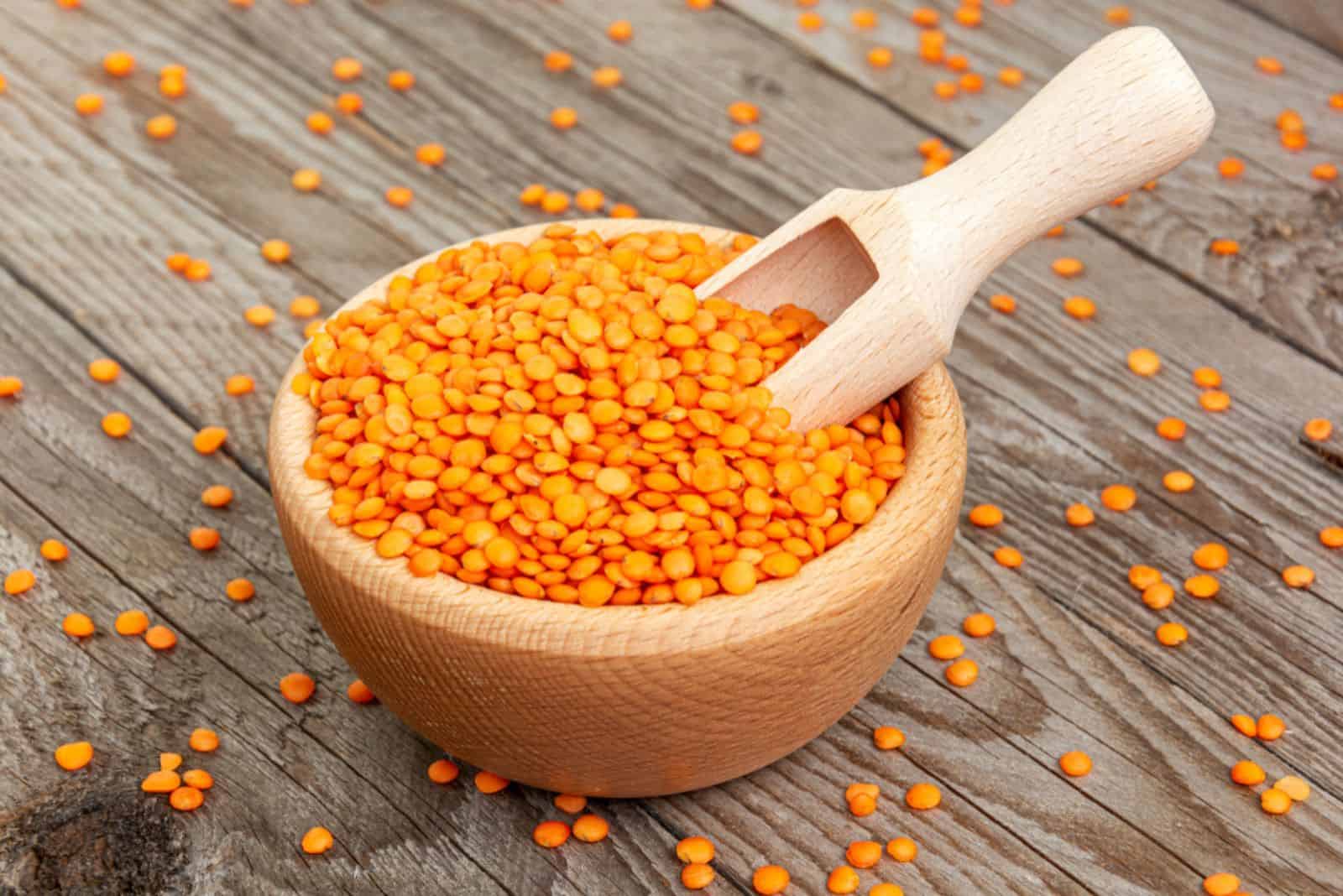 red lentils in wooden bowl with wooden measuring cup