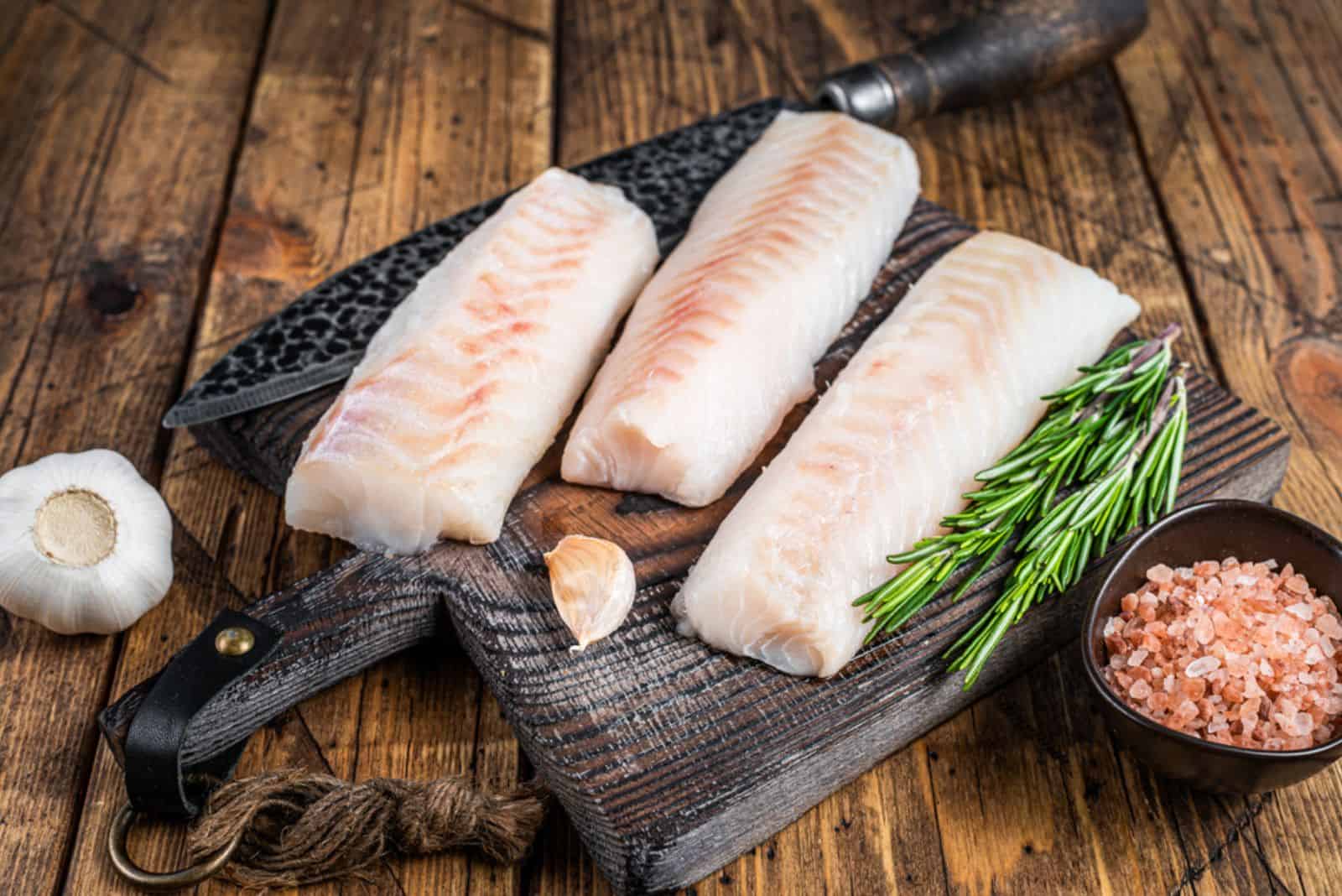 Tranci di filetto di merluzzo crudo fresco su tavola di legno con coltello da macellaio