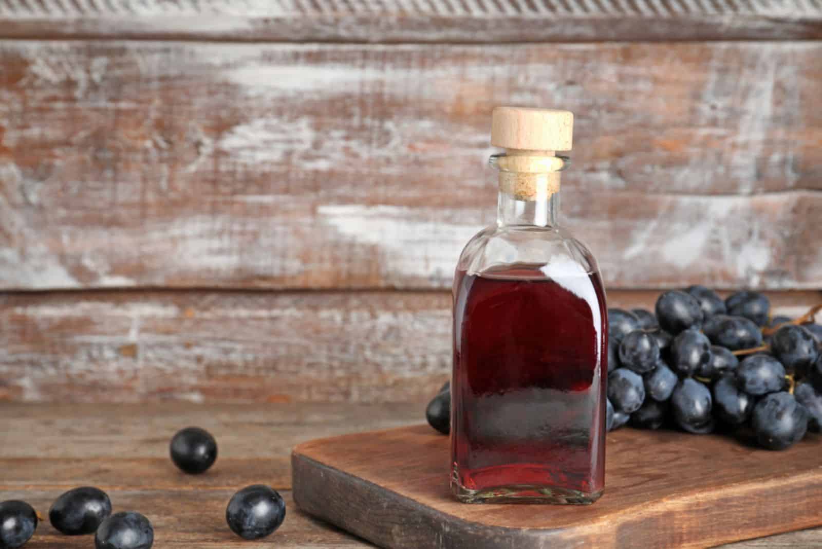 Botella de cristal con vinagre de vino y uvas frescas sobre mesa de madera