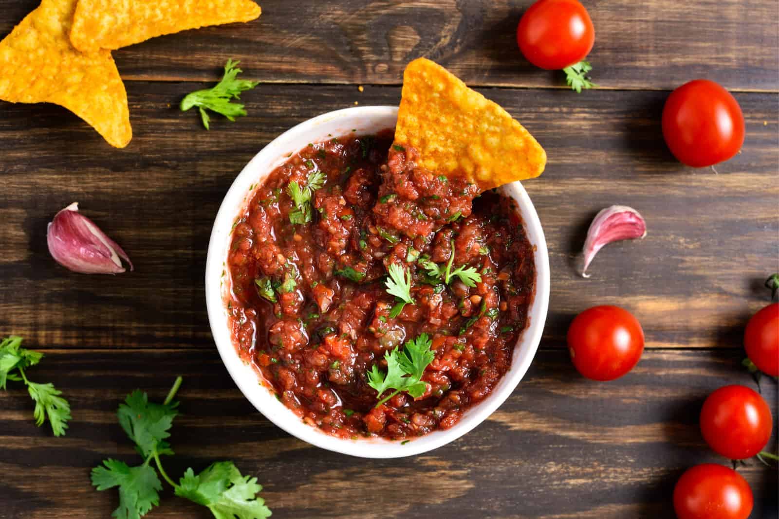 Homemade tomato salsa in bowl over wooden background