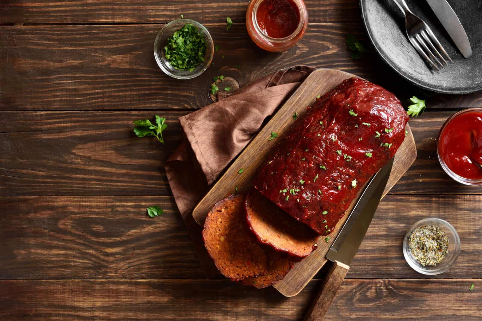 Meatloaf with glaze on cutting board over wooden background