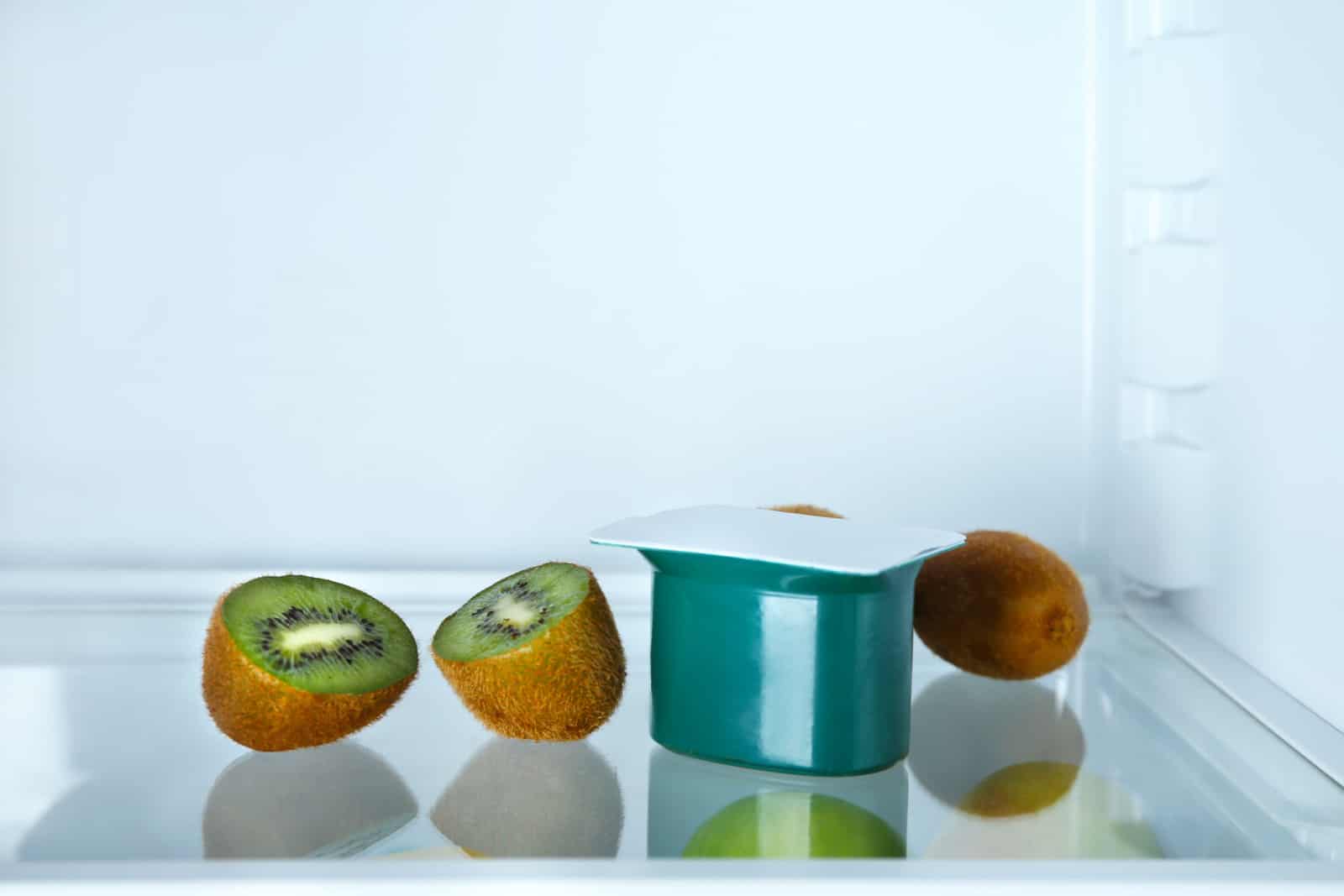 Plastic cup with yogurt and kiwi in refrigerator