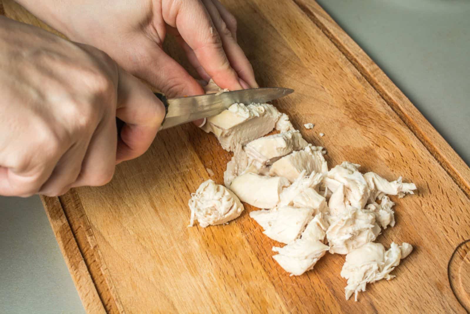 Tender hands of the girl cut with knife boiled chicken breast 