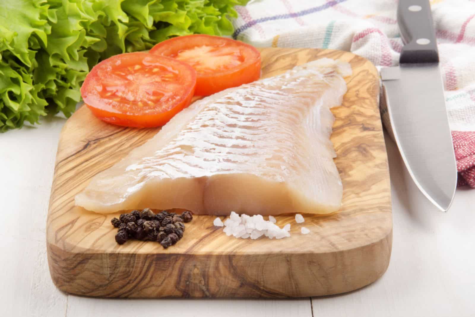 haddock fillet with tomato, pepper and coarse salt on a wooden board
