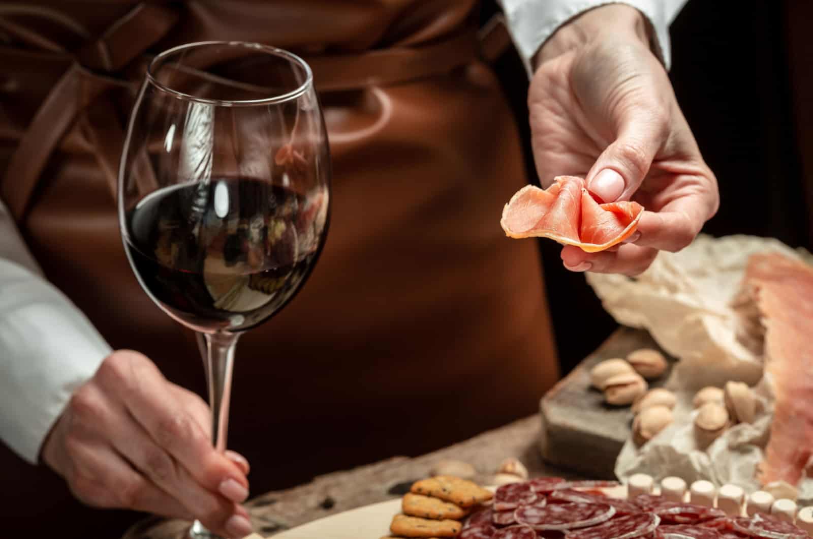 person holding a glass of wine and prosciutto