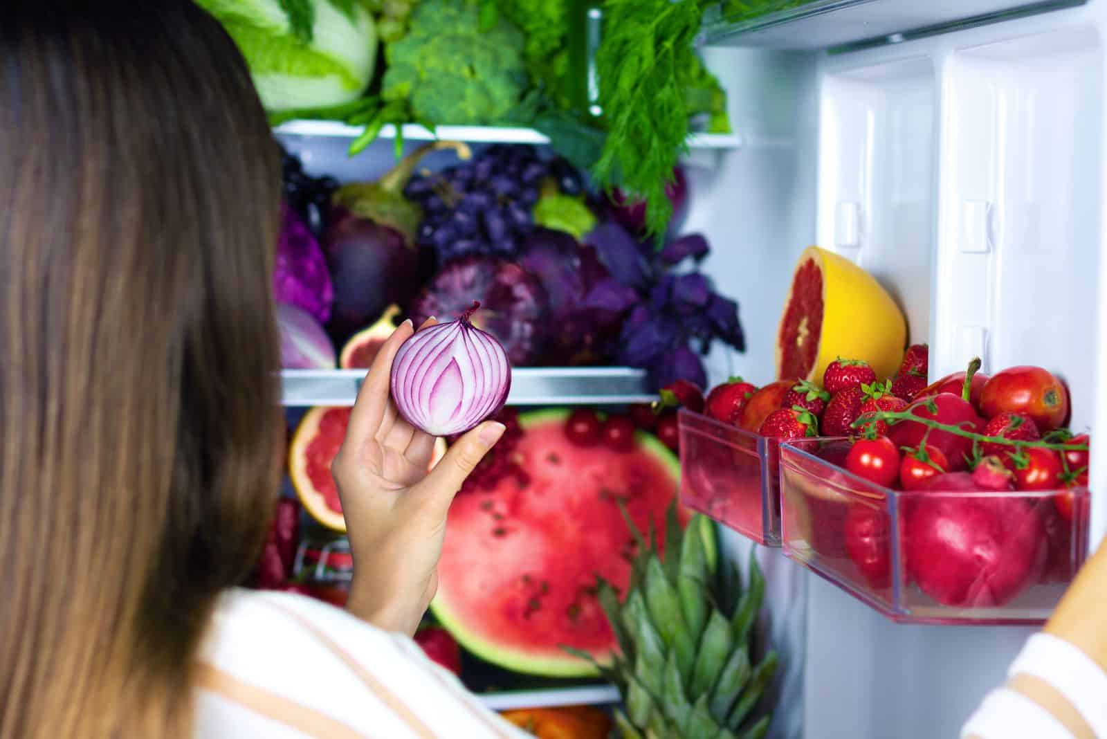 the woman takes out an onion from the refrigerator