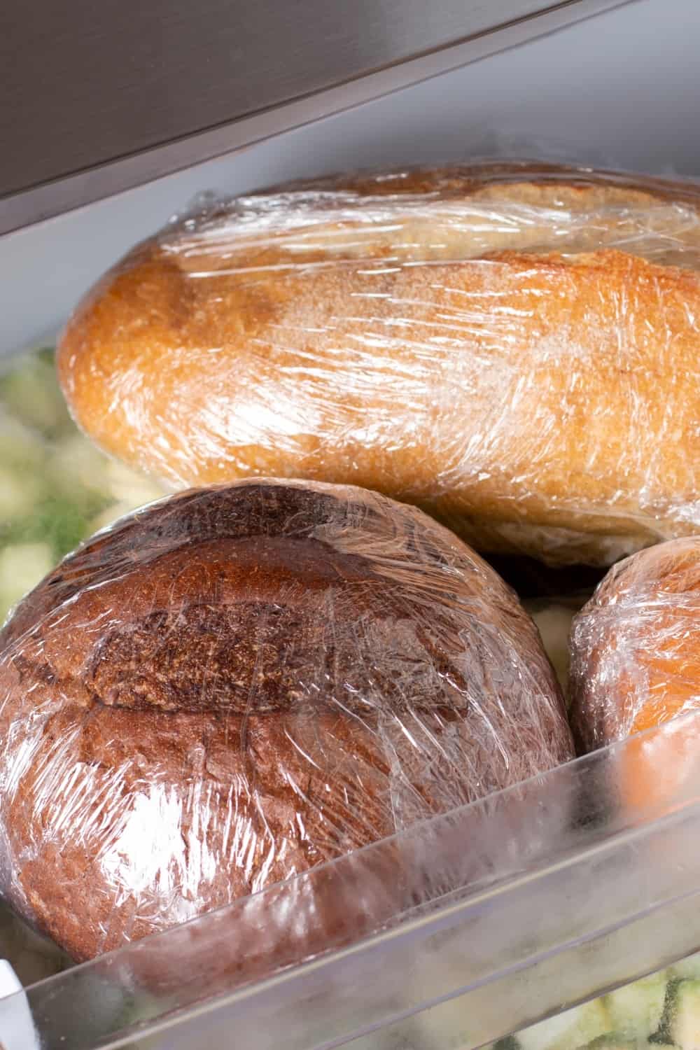 A loaf of wheat bread and other frozen food on a shelf of a home freezer