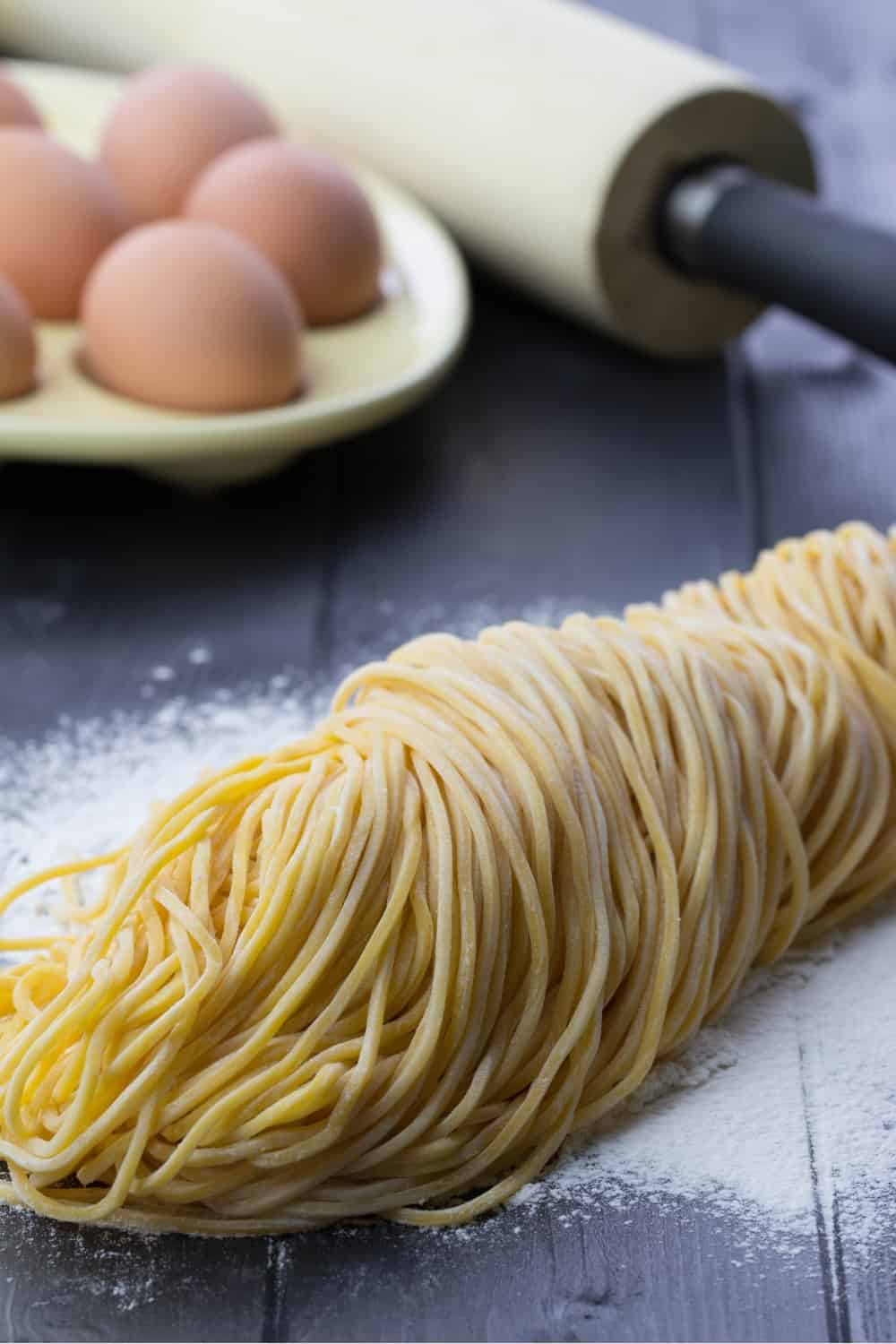 Homemade egg noodles with eggs, wheat flour and wooden rolling pin on the black wooden background