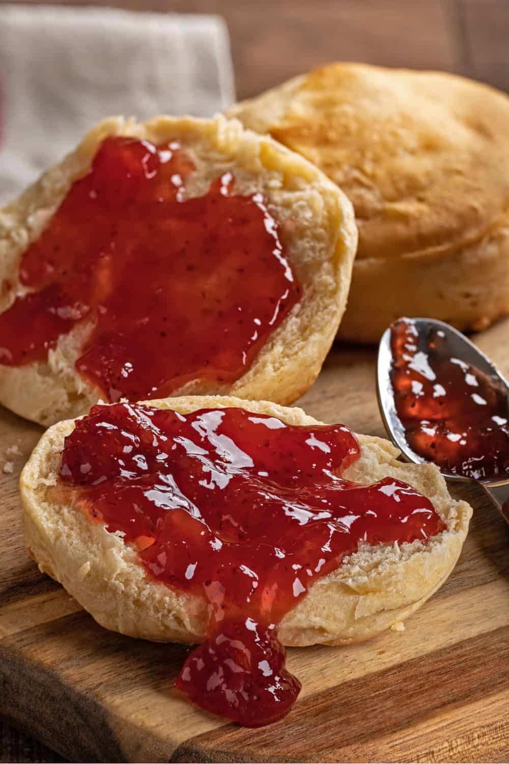 English muffin spread with strawberry preserves on a wooden cutting board