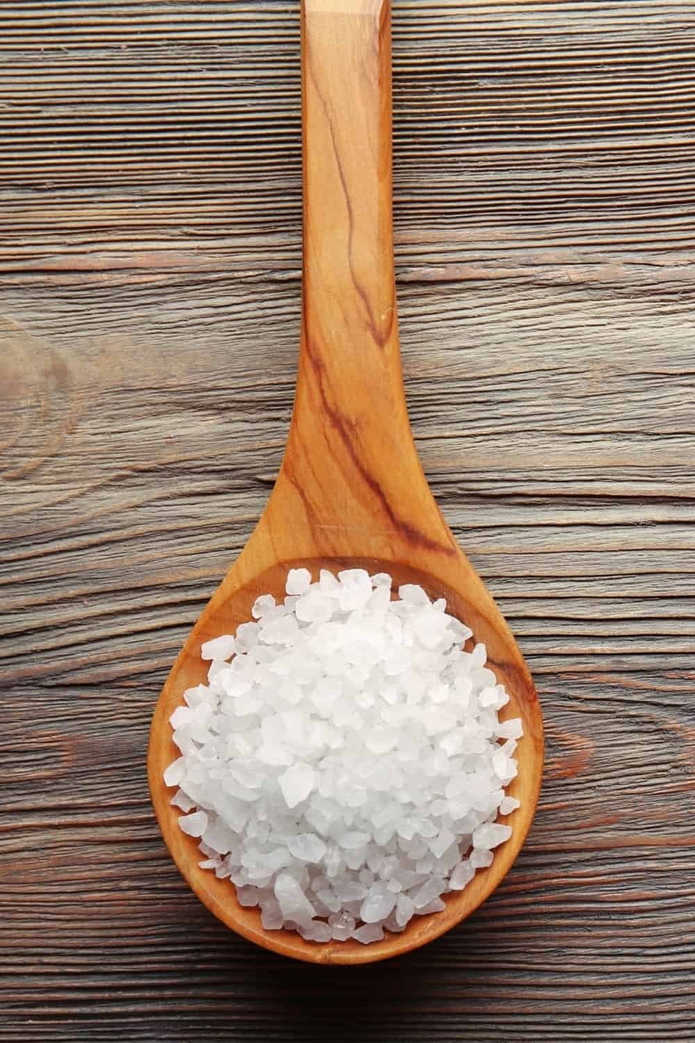 Spoon with sea salt on wooden background