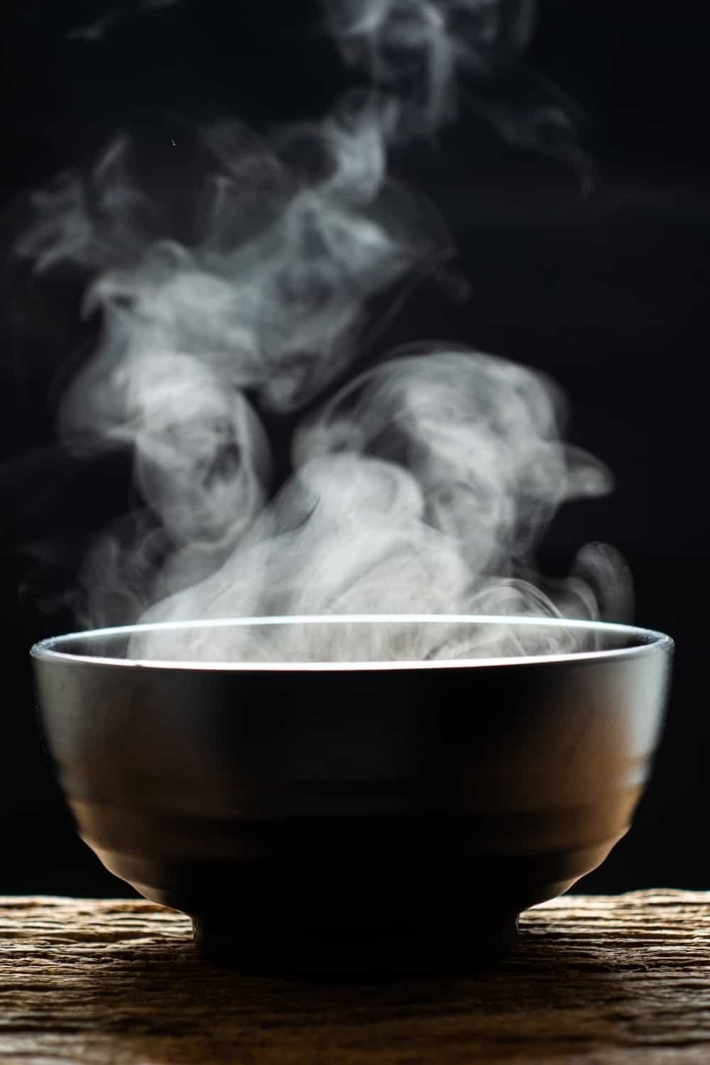 Steam of hot soup with smoke wood bowl on dark background
