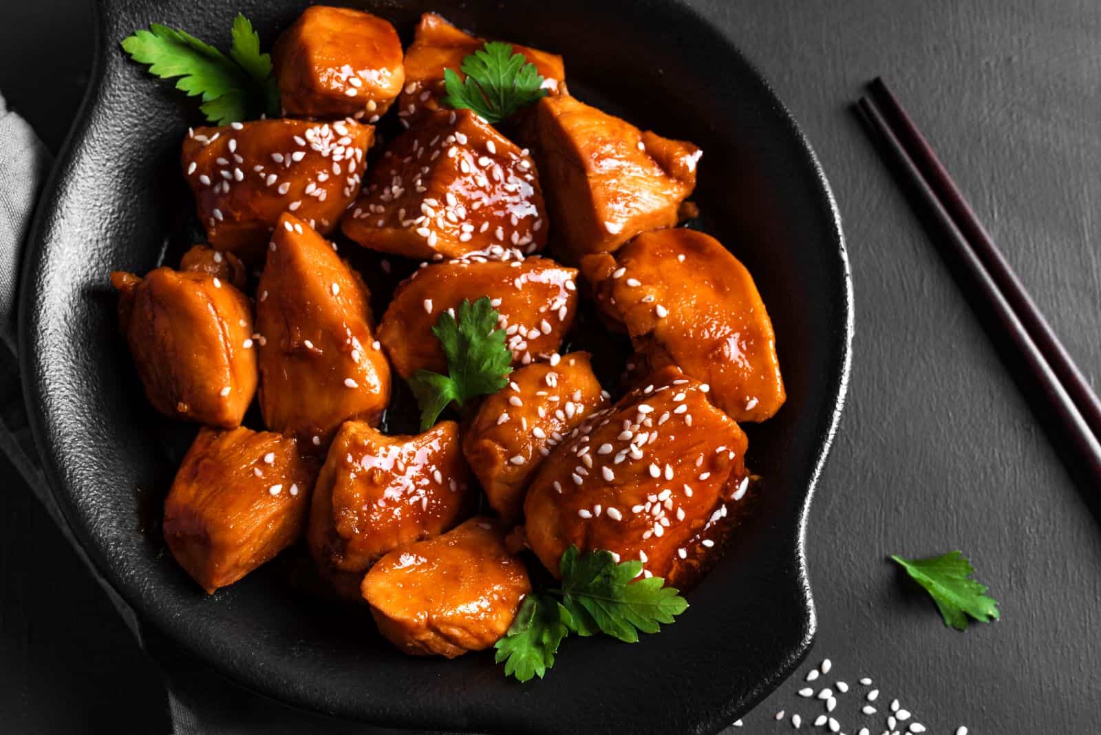 sesame chicken served in a black bowl with chopsticks