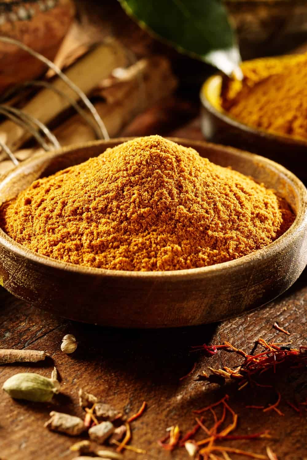 tavolo di legno con curry in polvere e curcuma intera e macinata in ciotole accanto a bastoncini di bambù