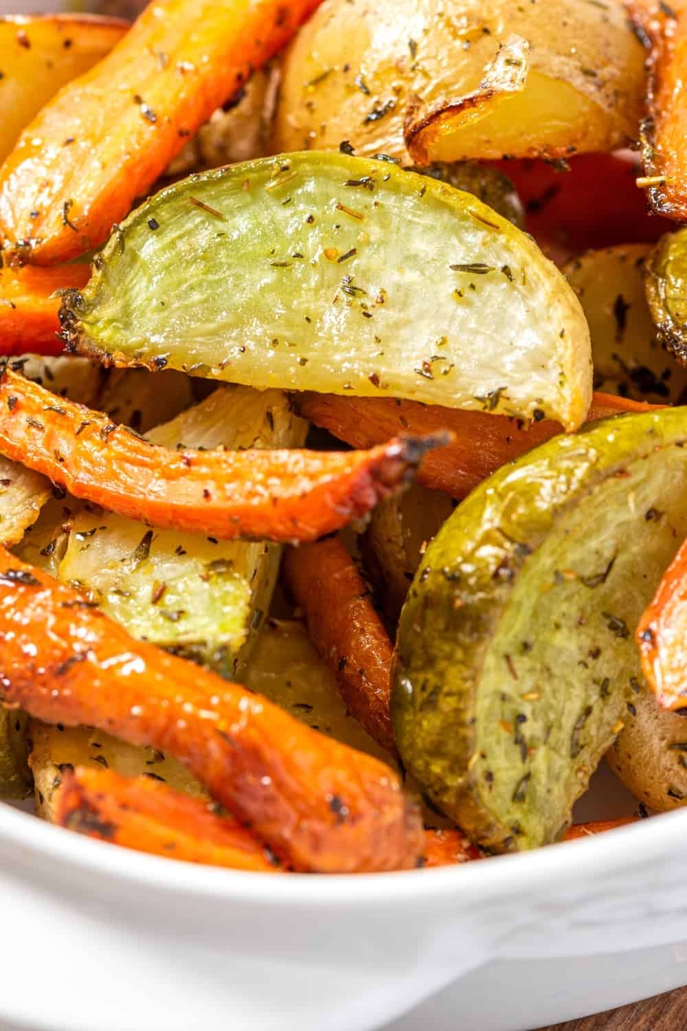 Legumes cozidos numa assadeira branca em grande plano. Batatas, cenouras e nabos fritos com azeite